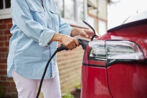 Close Up Of Woman Attaching Charging Cable To Electric Car At Home